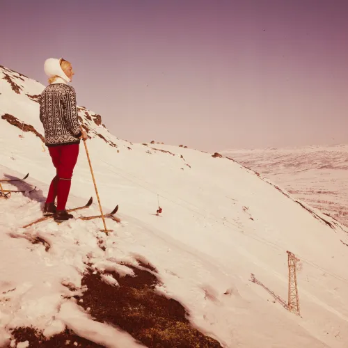 To damer i tidsriktige klær fra 1969 på ski på toppen av Hovden Skisenter. Nyter sol og utsikt.